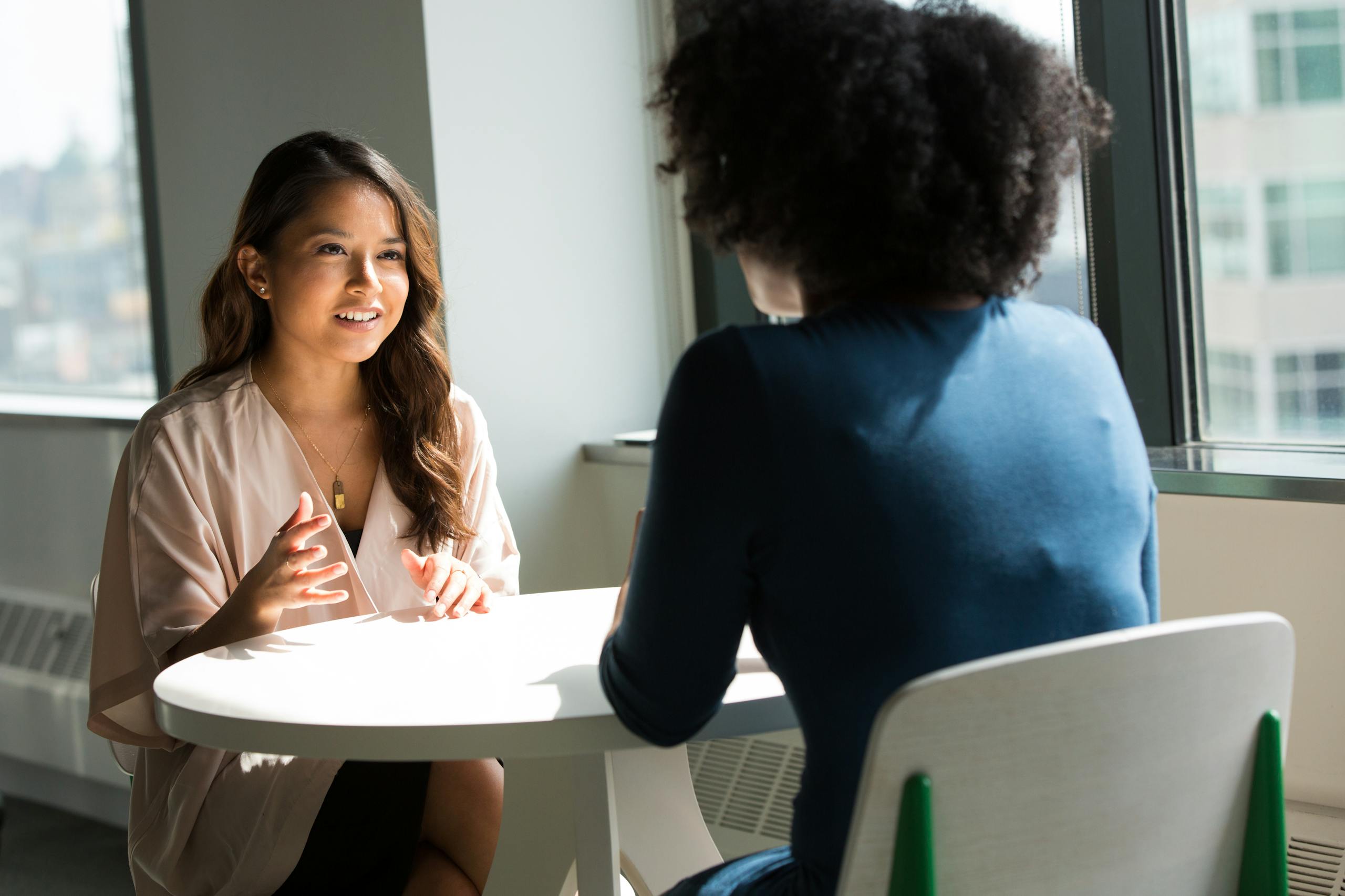 Two women sitting at table having professional discussion in bright office setting
