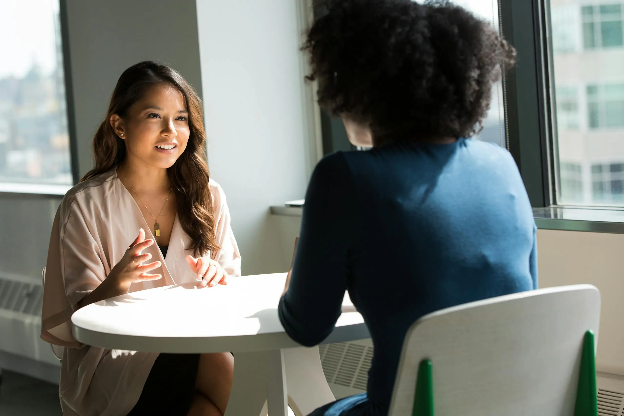 Two women sitting at table having professional discussion in bright office setting