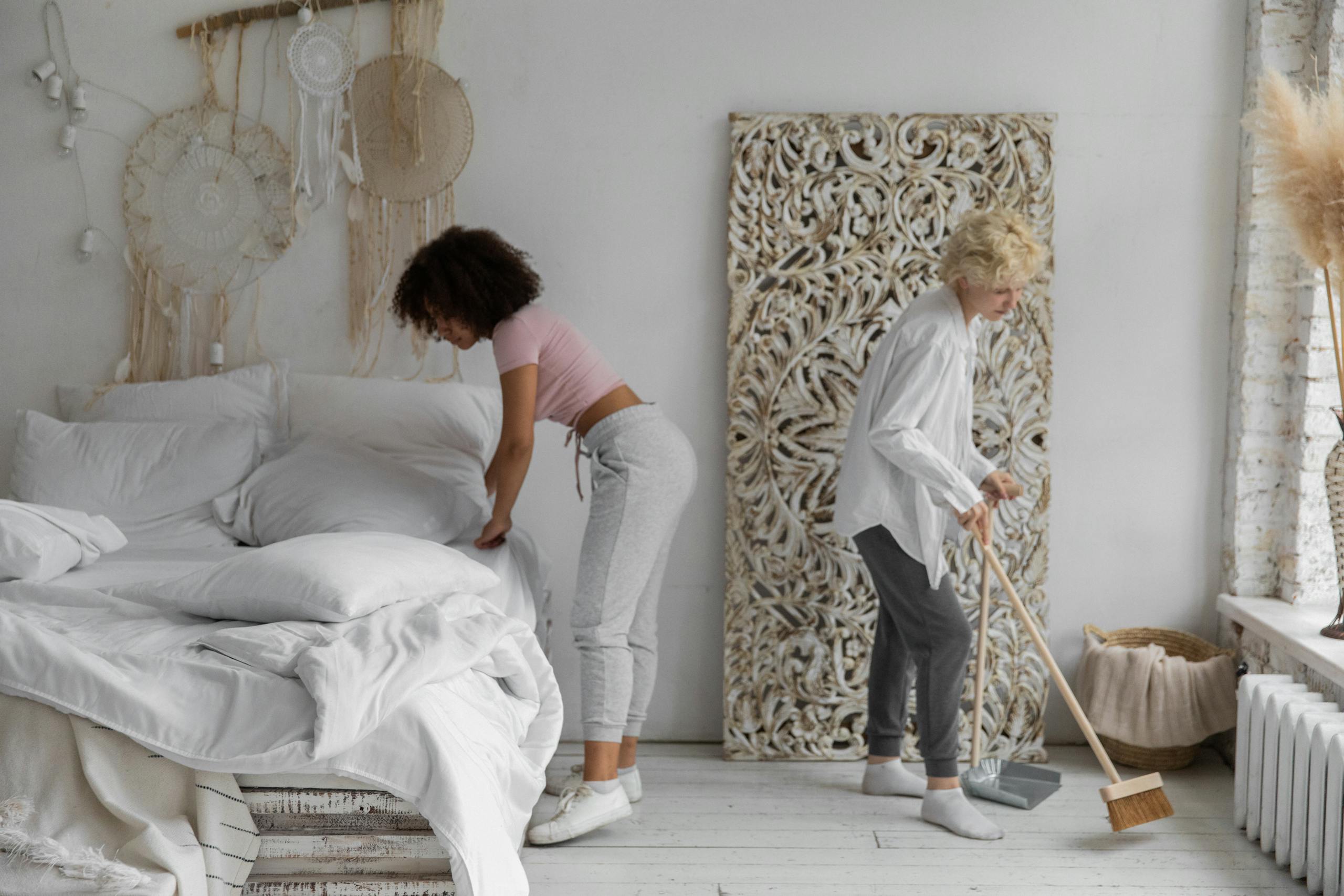Two women tidying contemporary bedroom with natural decor elements showing stylish organization.