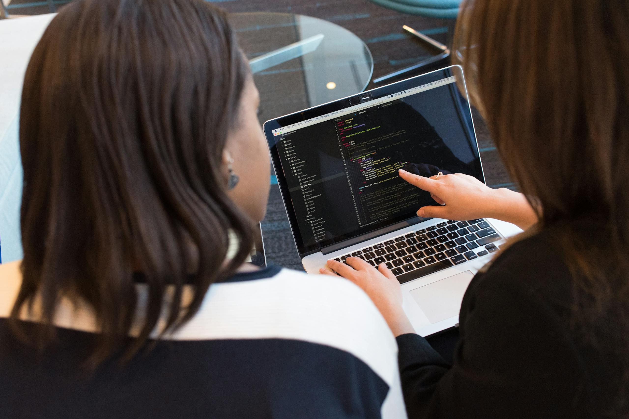 Two women collaboratively working on software programming code indoors together.