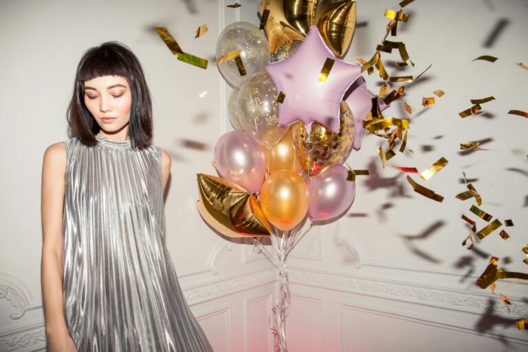 Contemplative woman in silver dress amid celebratory balloons and confetti
