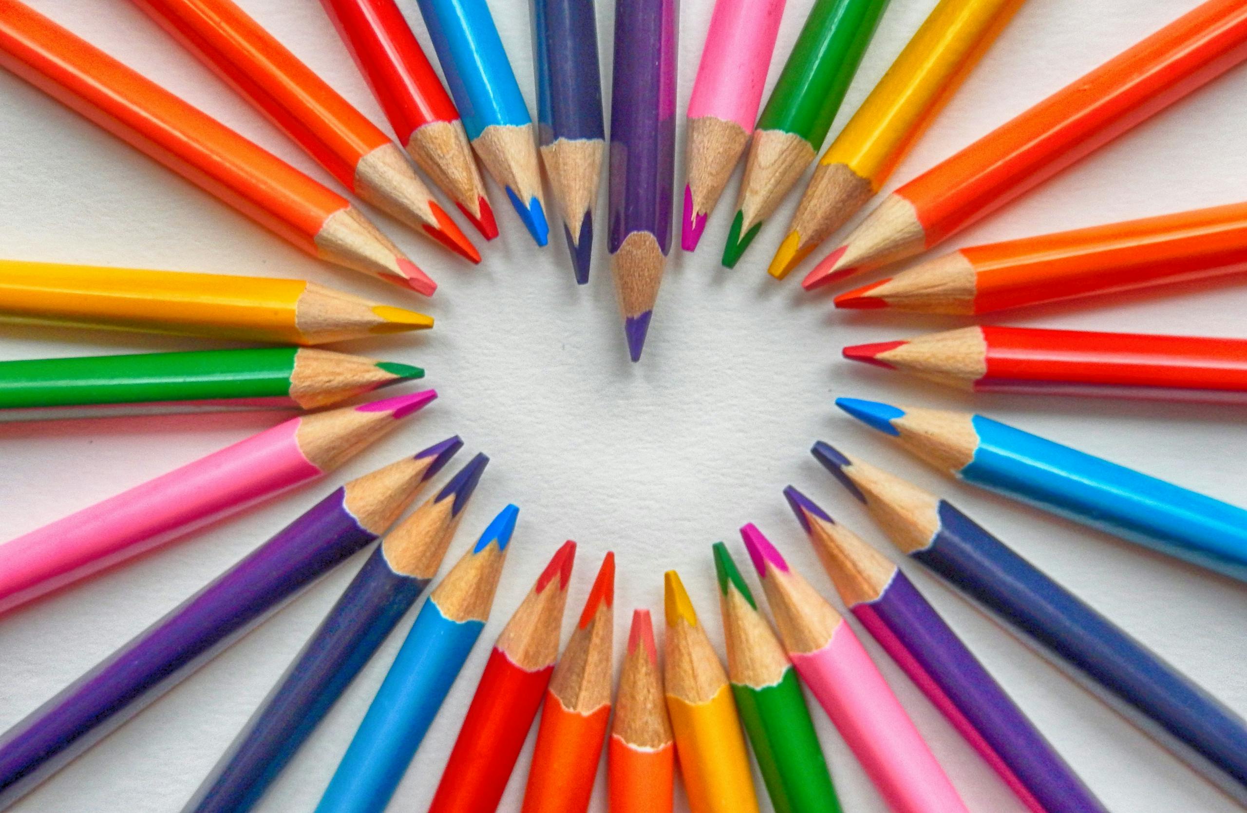 Vibrant colored pencils arranged in heart shape on white background.