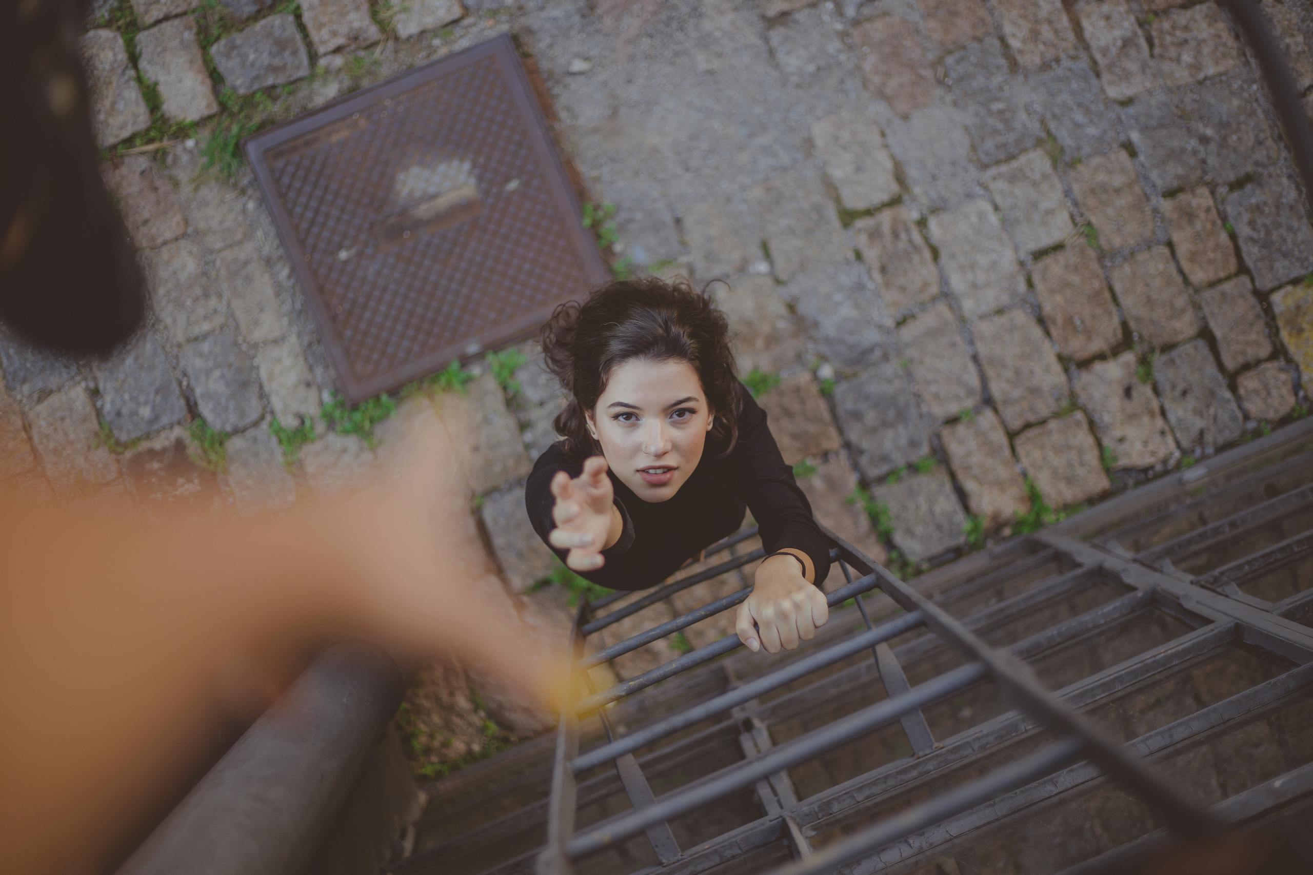 Woman climbs iron ladder outdoors reaching upward with determination and effort.