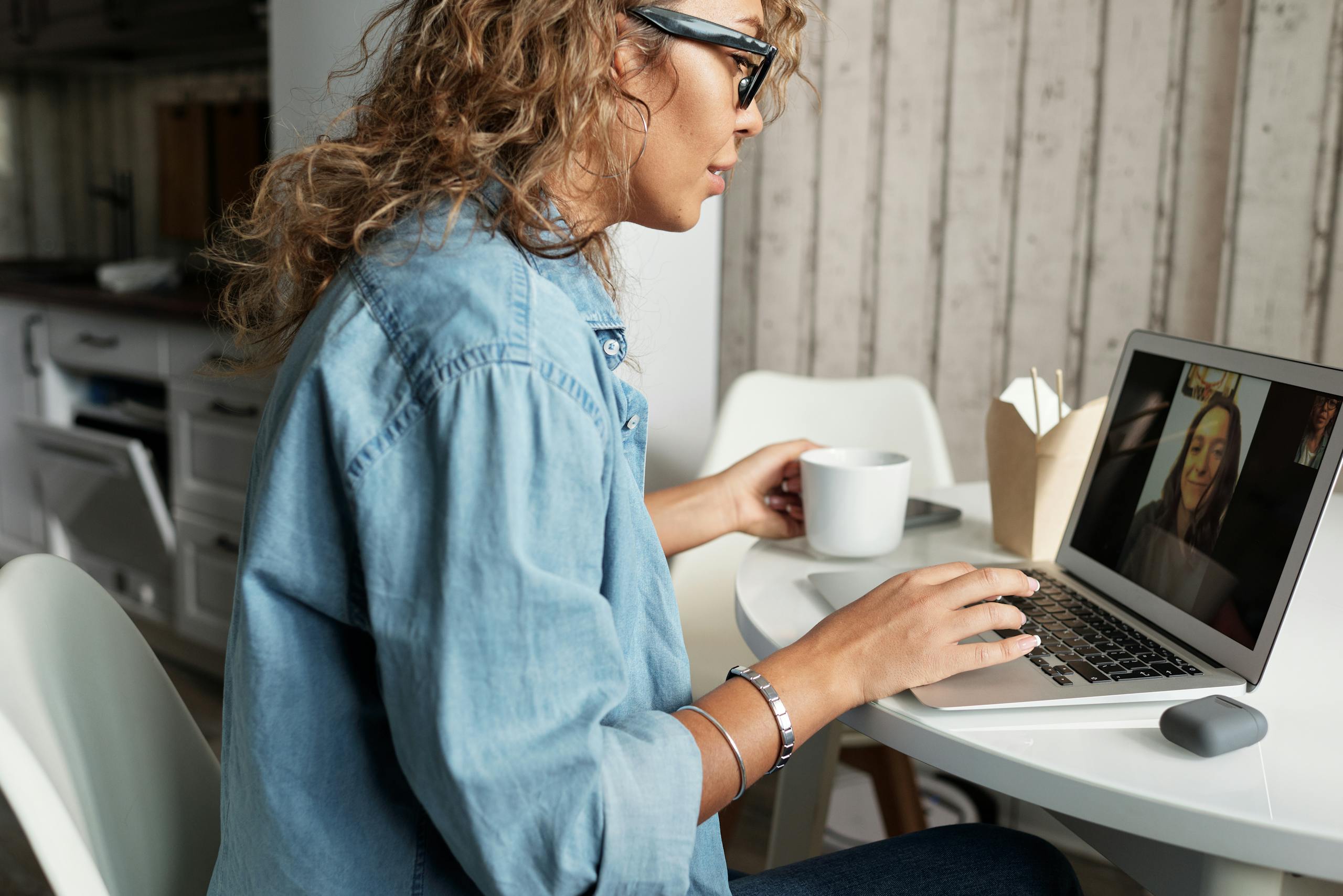 Woman enjoying video call with friend at home sipping coffee