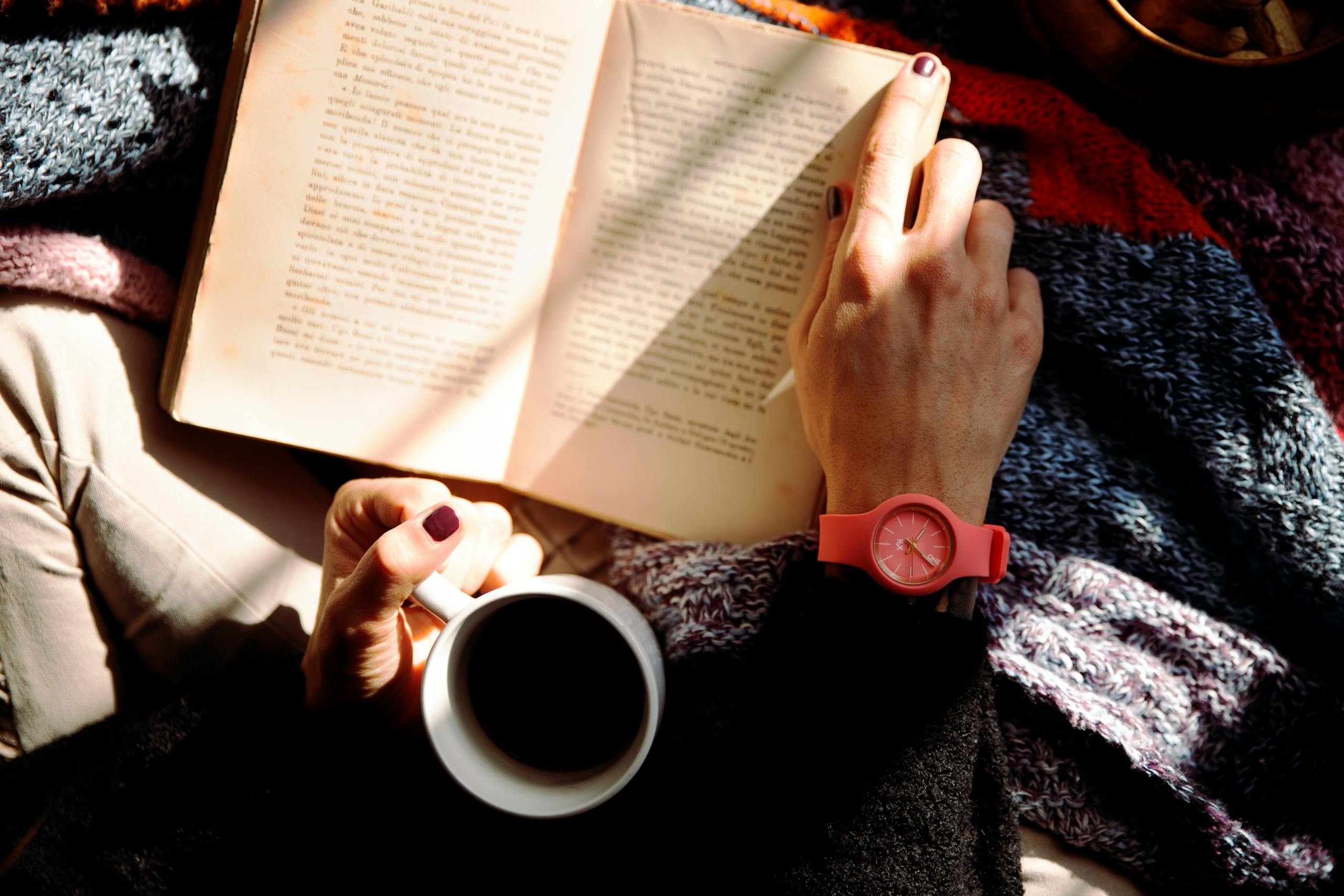 Woman relaxing with book and coffee in sunlit cozy space wearing watch.