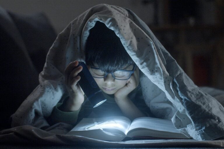 Young child enjoying bedtime story under blanket with flashlight.
