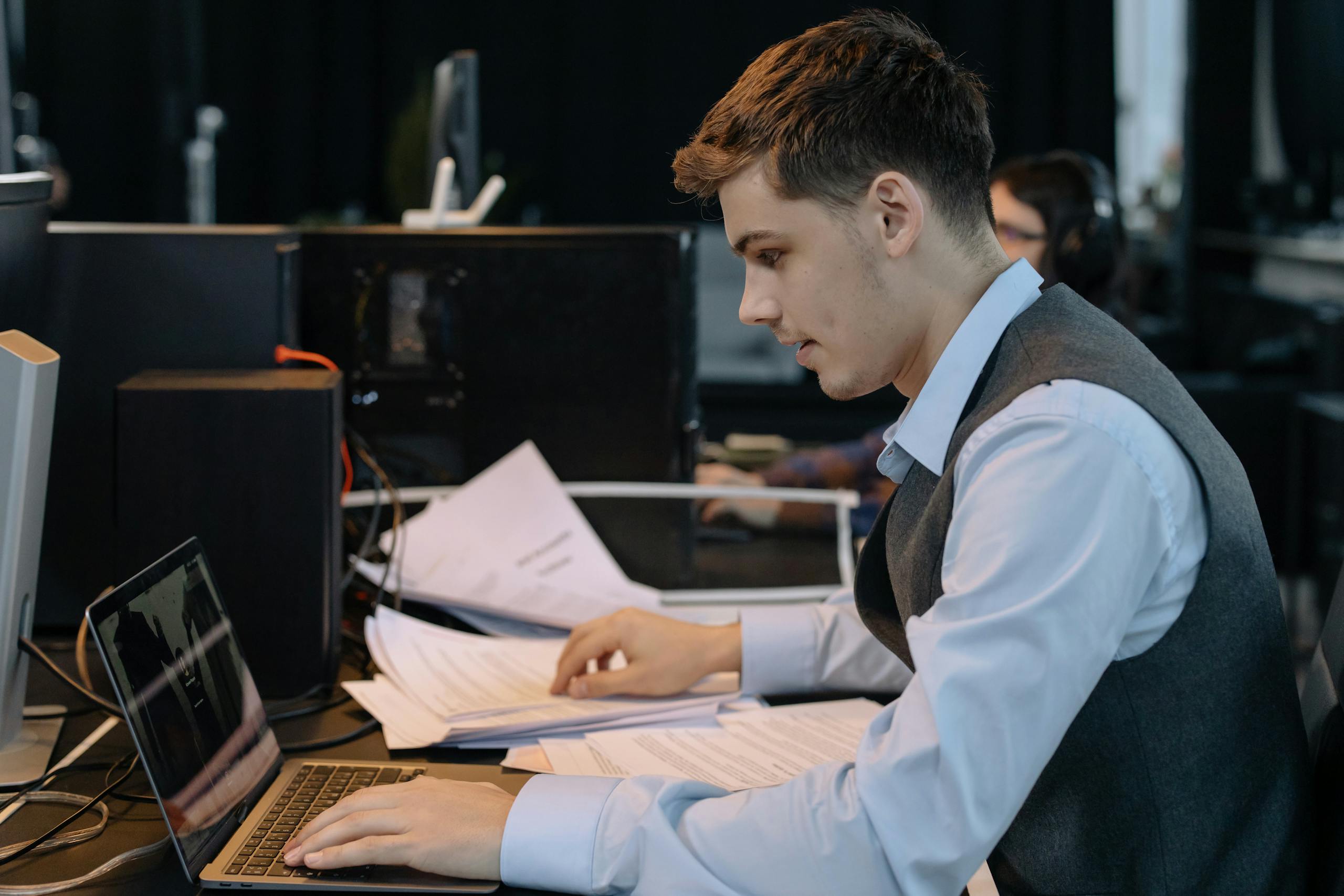 Young male professional concentrating on laptop work with documents at office desk