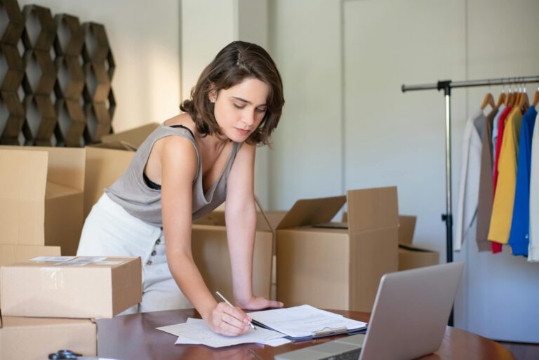 Young woman managing online clothing business from home office with boxes and laptop