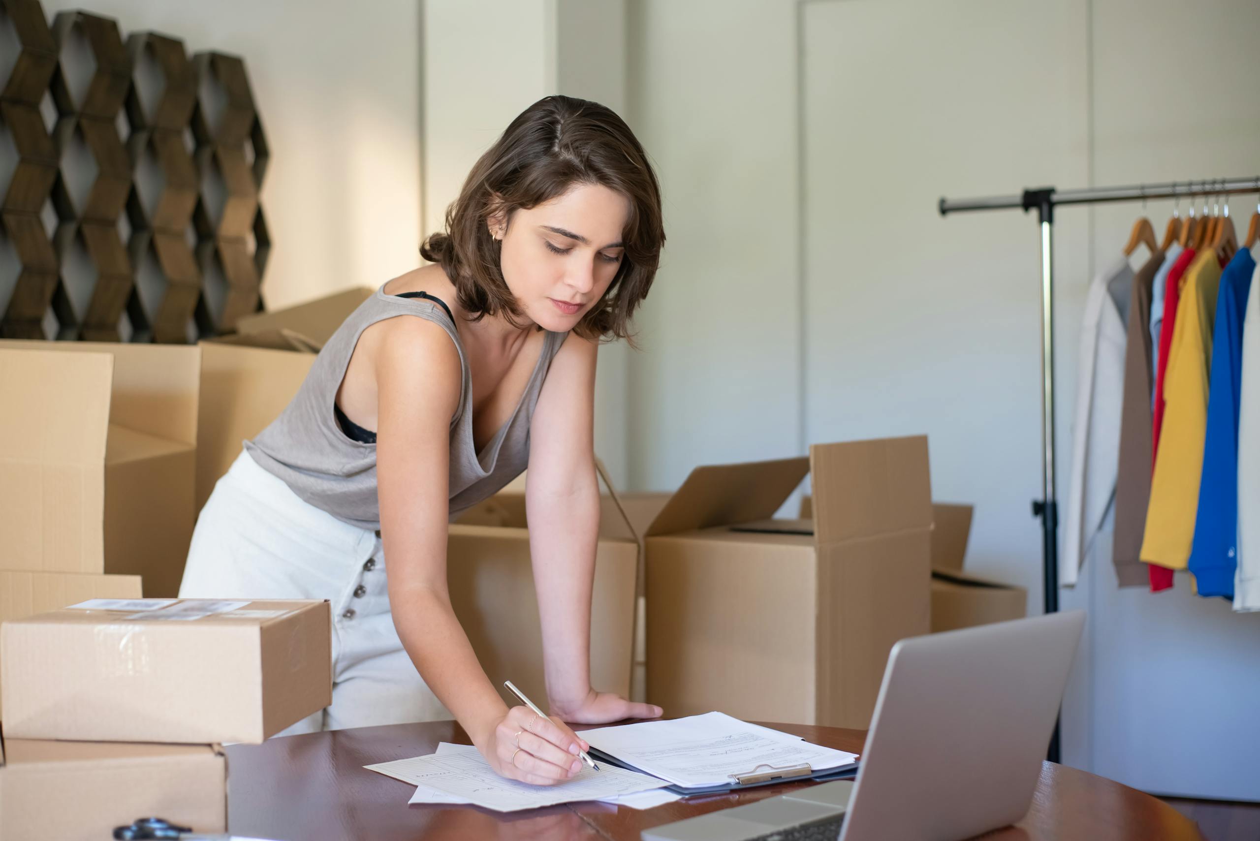 Young woman managing online clothing business from home office with boxes and laptop