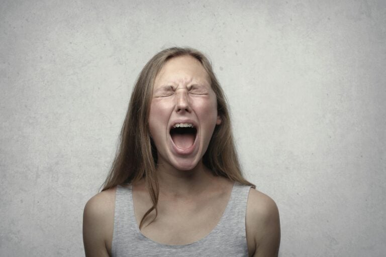 Young woman screaming with emotion showing braces against gray backdrop.