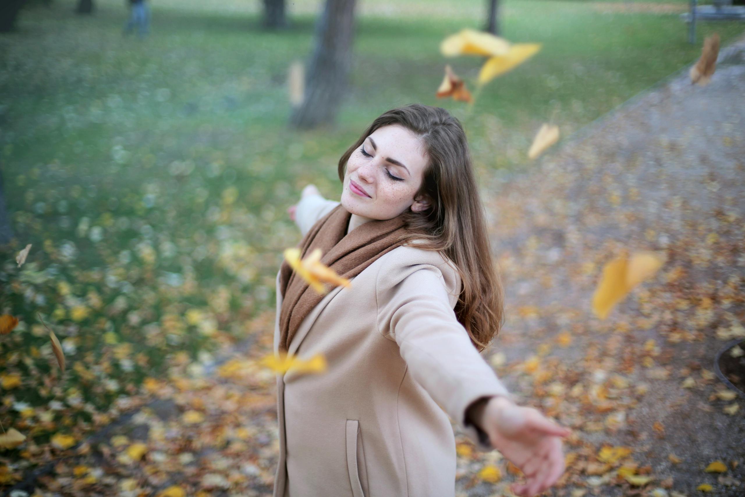 Young woman with outstretched arms delighting in fallen autumn leaves in Paris park