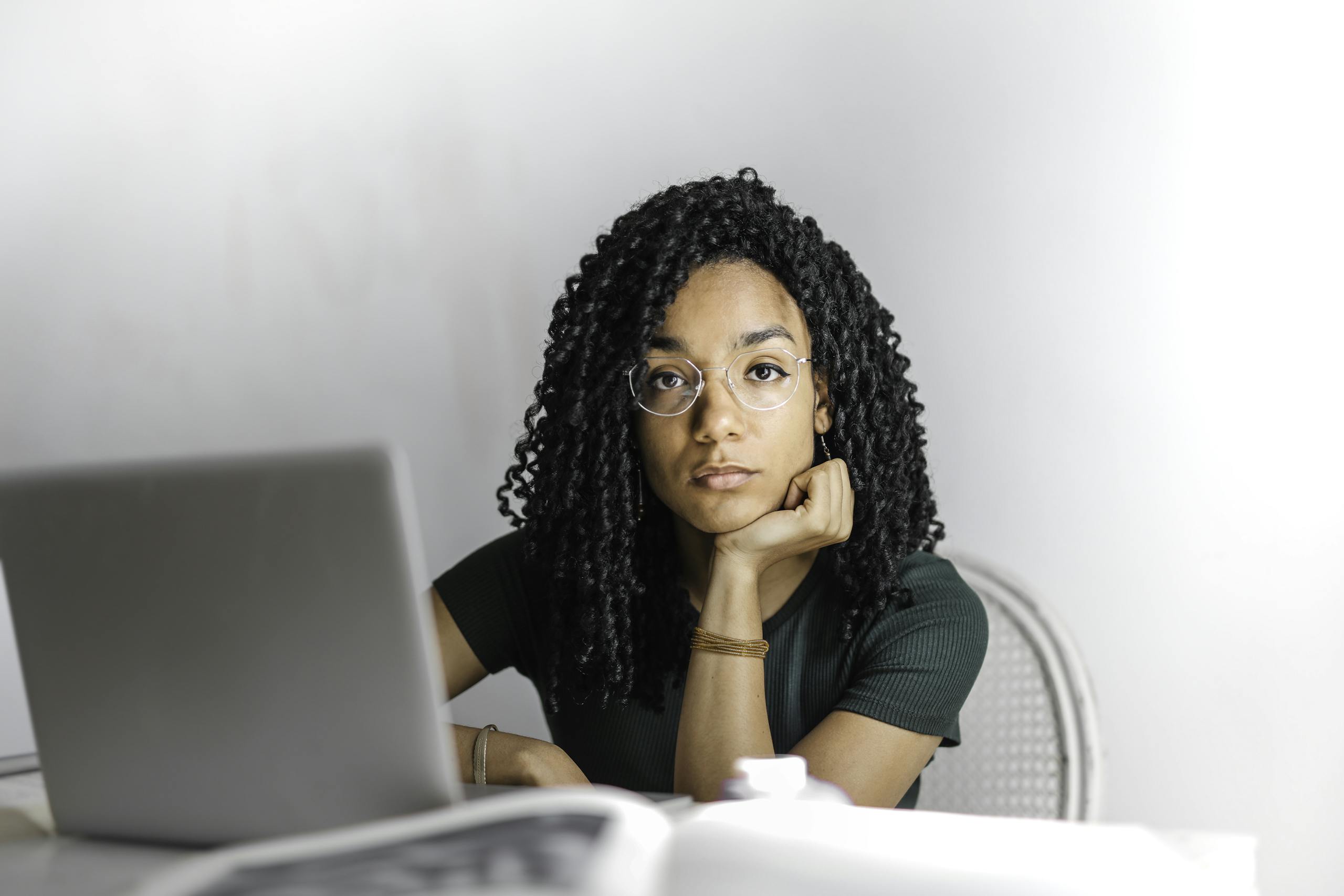 Young woman with glasses works attentively on laptop at bright desk.